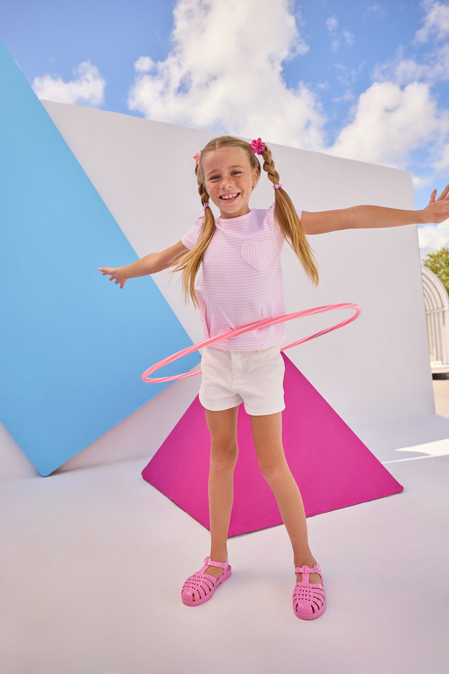 Model can be seen wearing Girls/Tween short sleeve knit top in a light pink and white stripe. Top also features a faux heart pocket to elevate the tee. Paired back perfectly with ivory denim shorts to complete the look. 