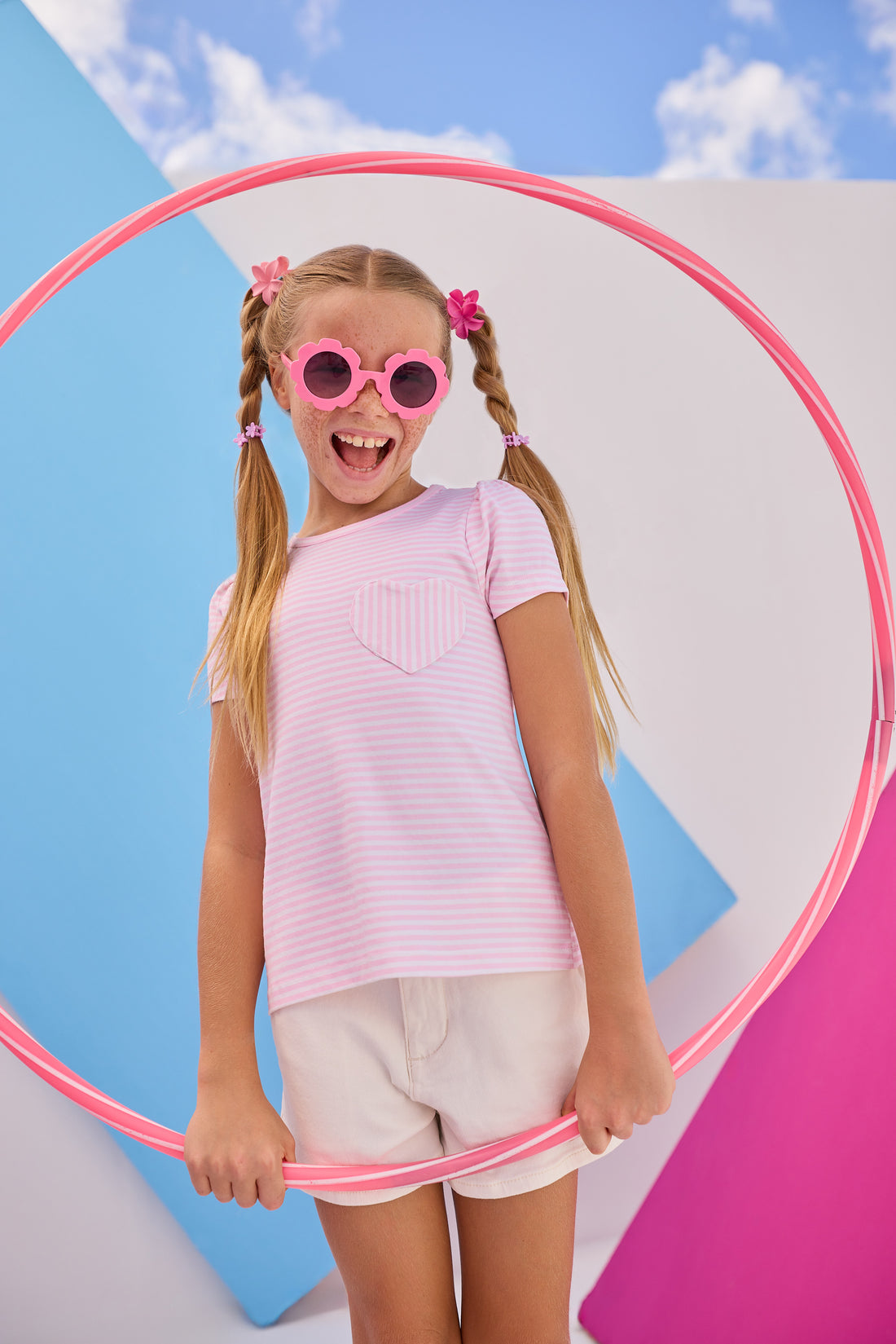 Model can be seen wearing Girls/Tween short sleeve knit top in a light pink and white stripe. Top also features a faux heart pocket to elevate the tee. Paired back perfectly with ivory denim shorts to complete the look. 