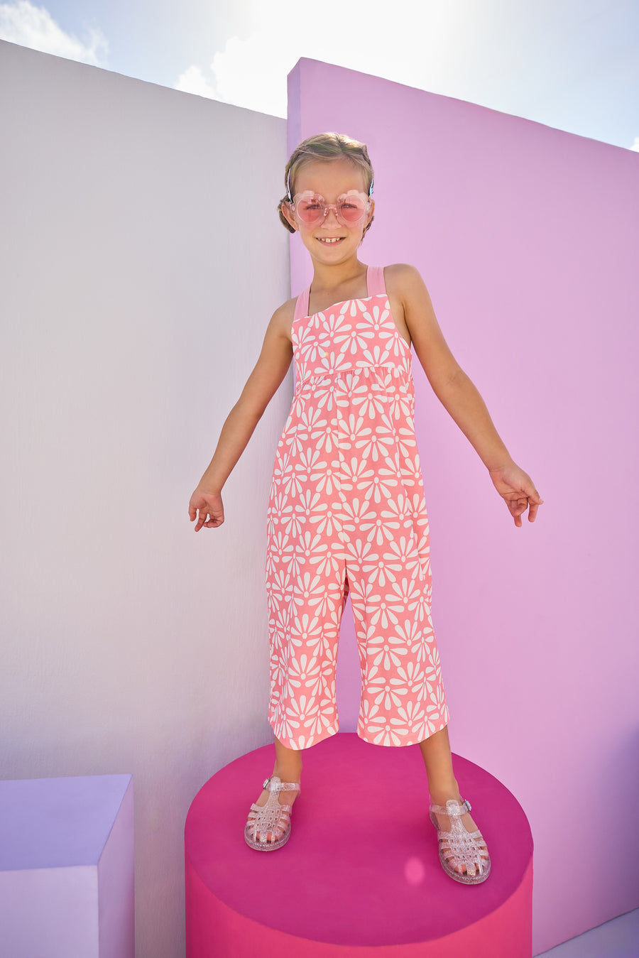 Girls/Tween model can be seen in knit jumpsuit in a salmon/pink and white floral print.This jumpsuit has adjustable woven straps and pockets for easy relaxed fit.