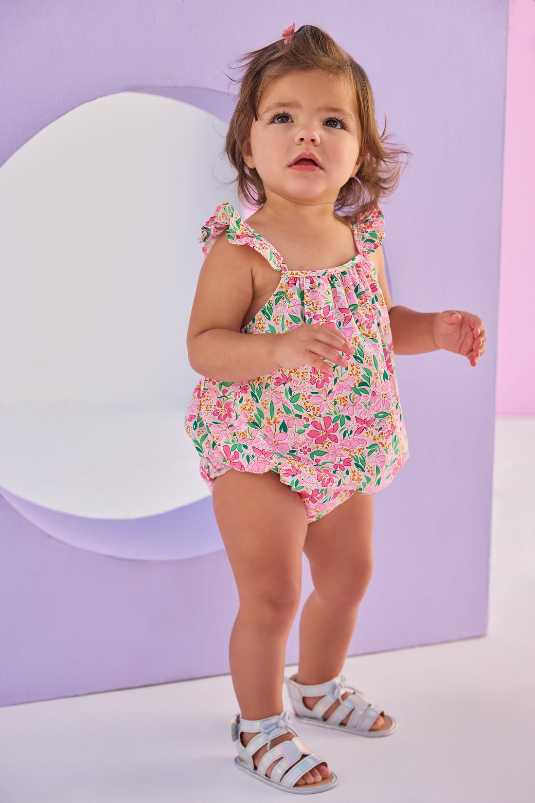 Baby girl woven bubble in a hot pink/yellow/green floral pattern. Bubble features button closures along back and stride and strappy angel sleeves for an elevated look.