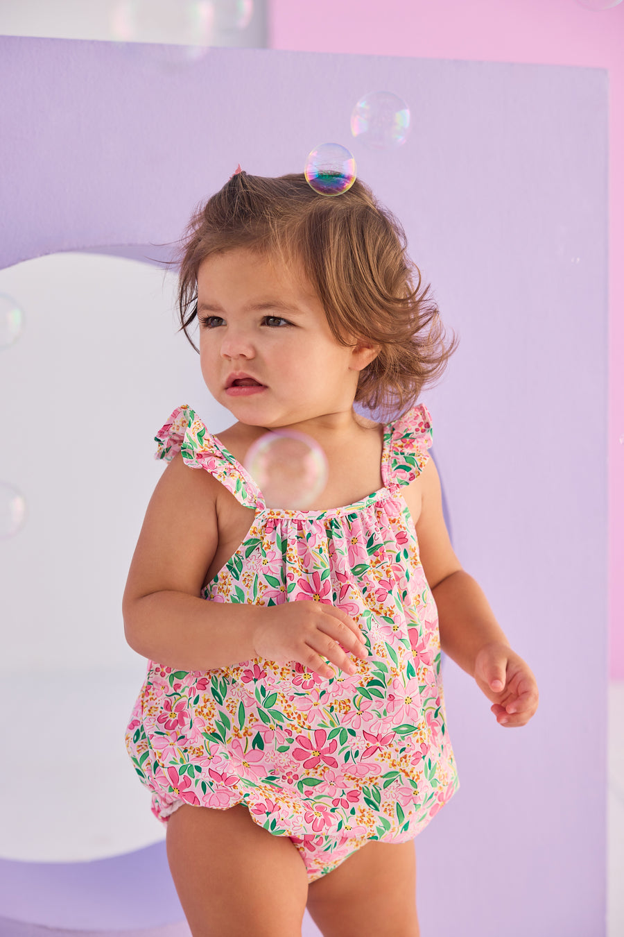 Baby girl woven bubble in a hot pink/yellow/green floral pattern. Bubble features button closures along back and stride and strappy angel sleeves for an elevated look.