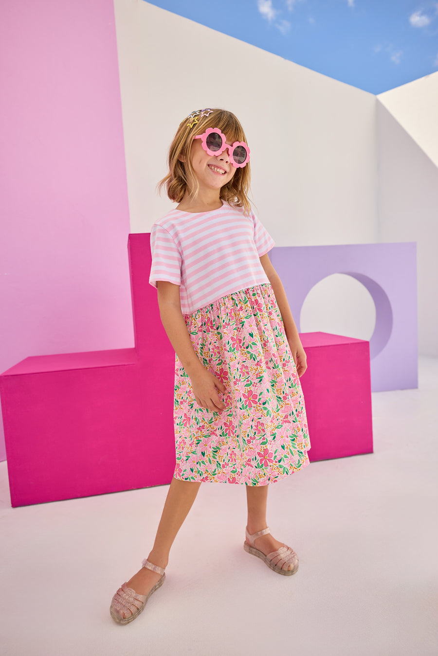 Model can be seen wearing a half knit half woven dress with knit pink/white stripe top half and a woven skirt with pink/yellow floral print. There is also a three button closure along back for a relaxed but secure fit.