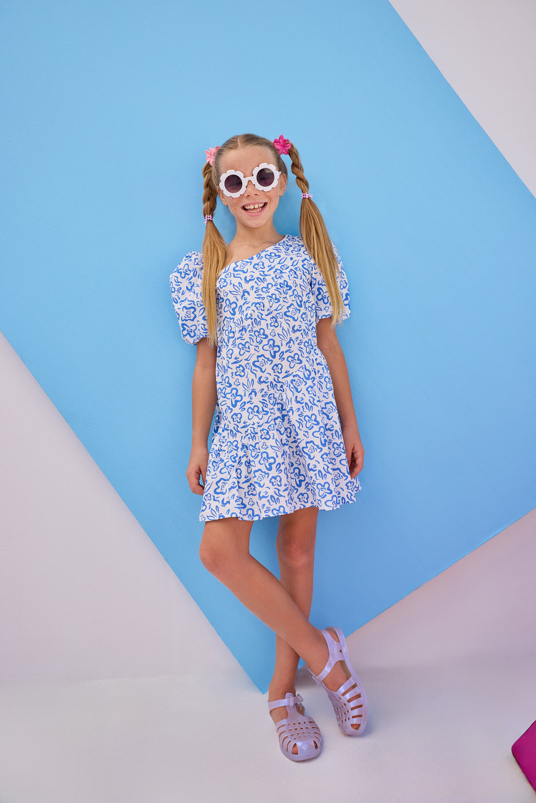 Model can be seen wearing  a woven dress in a royal blue and white floral pattern. Dress features a fun asymmetrical hem which adds a fun feature to the dress. Dress also has slight puff sleeves and also has a keyhole button closure on back of neckline. 