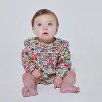 Babygirl long sleeve bubble with elastic wristband featuring a ruffle neckline and button closures along the back and stride in a vibrant magenta/pink/orange/green floral print.