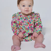 Babygirl long sleeve bubble with elastic wristband featuring a ruffle neckline and button closures along the back and stride in a vibrant magenta/pink/orange/green floral print.