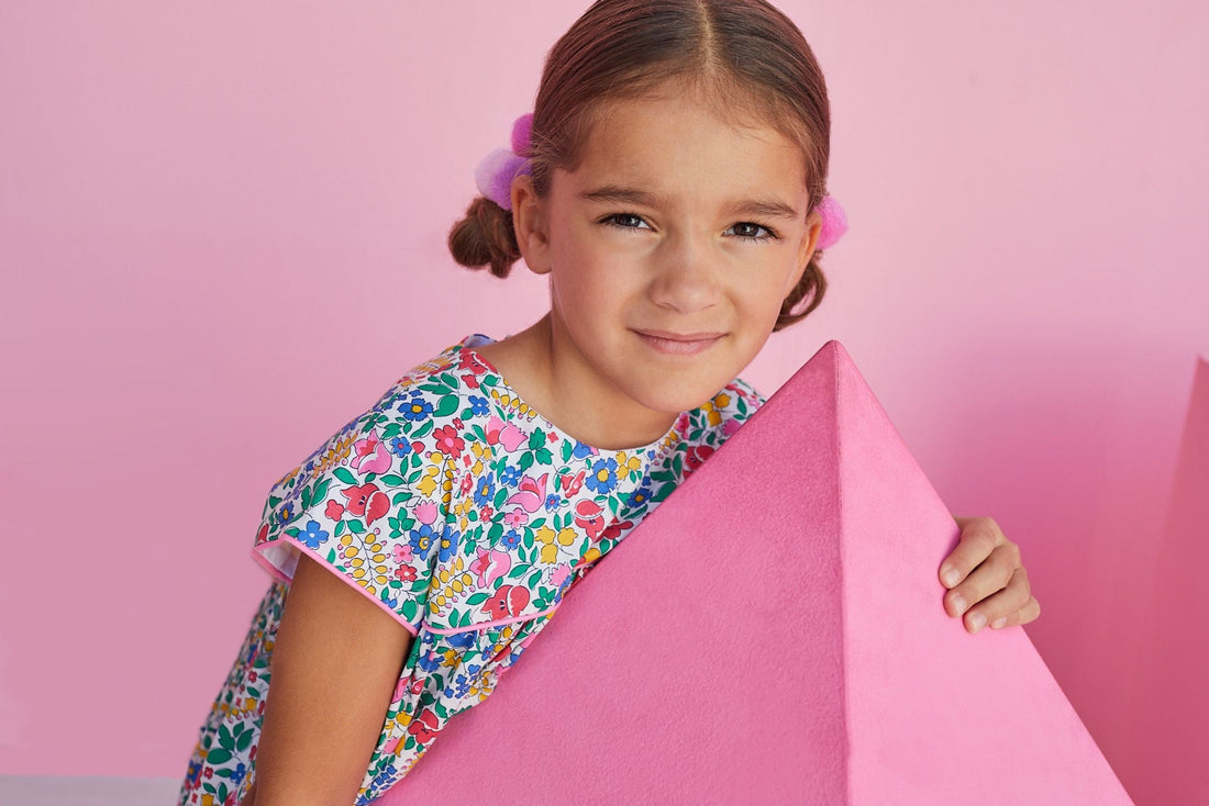 Young girl wearing BISBY Charlotte dress with vibrant flower pattern and light pink piping.