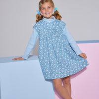 Girls short sleeve dress in blue/green/white floral print with aqua trim detailing that has button closures along back paired with a light blue turtleneck underneath.