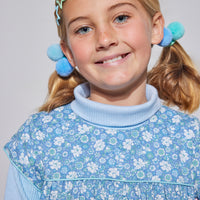 Girls short sleeve dress in blue/green/white floral print with aqua trim detailing that has button closures along back paired with a light blue turtleneck underneath.