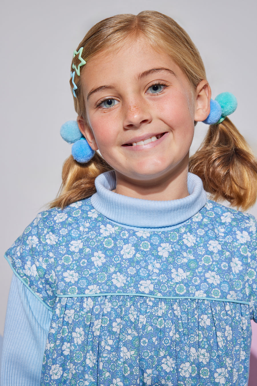 Girls short sleeve dress in blue/green/white floral print with aqua trim detailing that has button closures along back paired with a light blue turtleneck underneath.