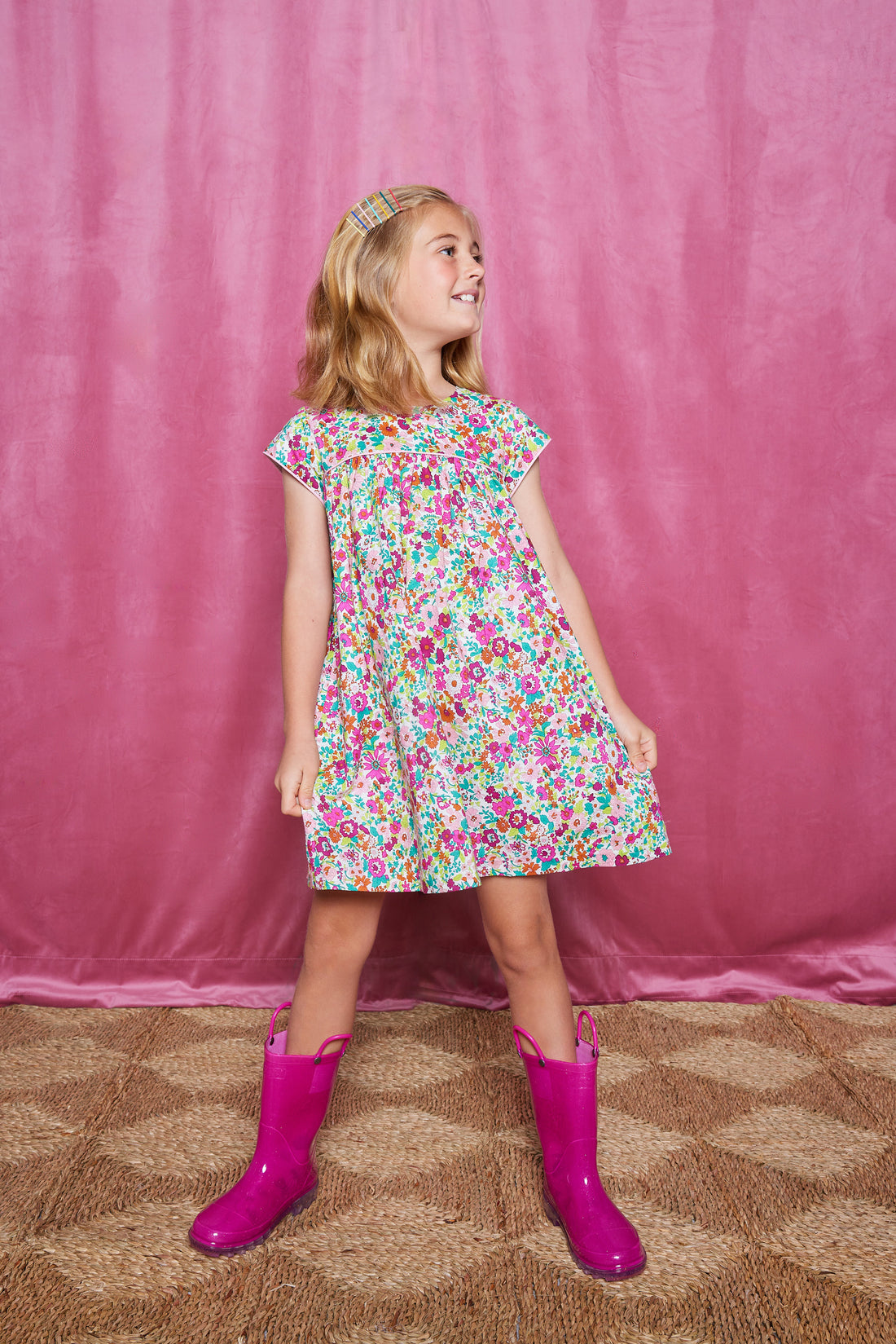 Girls short sleeve dress in magenta/pink/orange/green floral print with light pink trim detail and button closures along back.