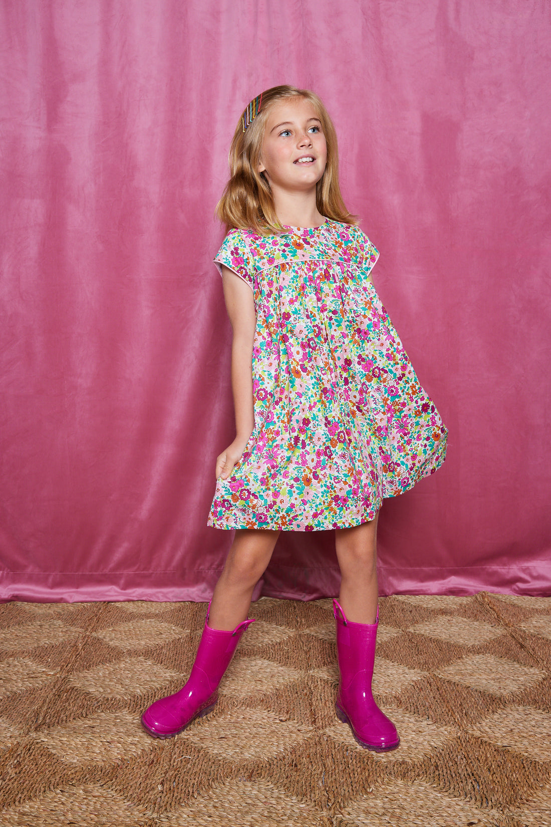 Girls short sleeve dress in magenta/pink/orange/green floral print with light pink trim detail and button closures along back.