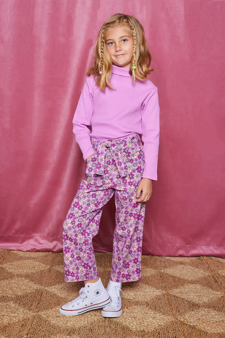 Tween woven pant with pockets  in a purple/magenta/pink floral pattern that comes with a belt in the matching print and button/zipper closure in front of pants paired back with a magenta ribbed turtleneck.