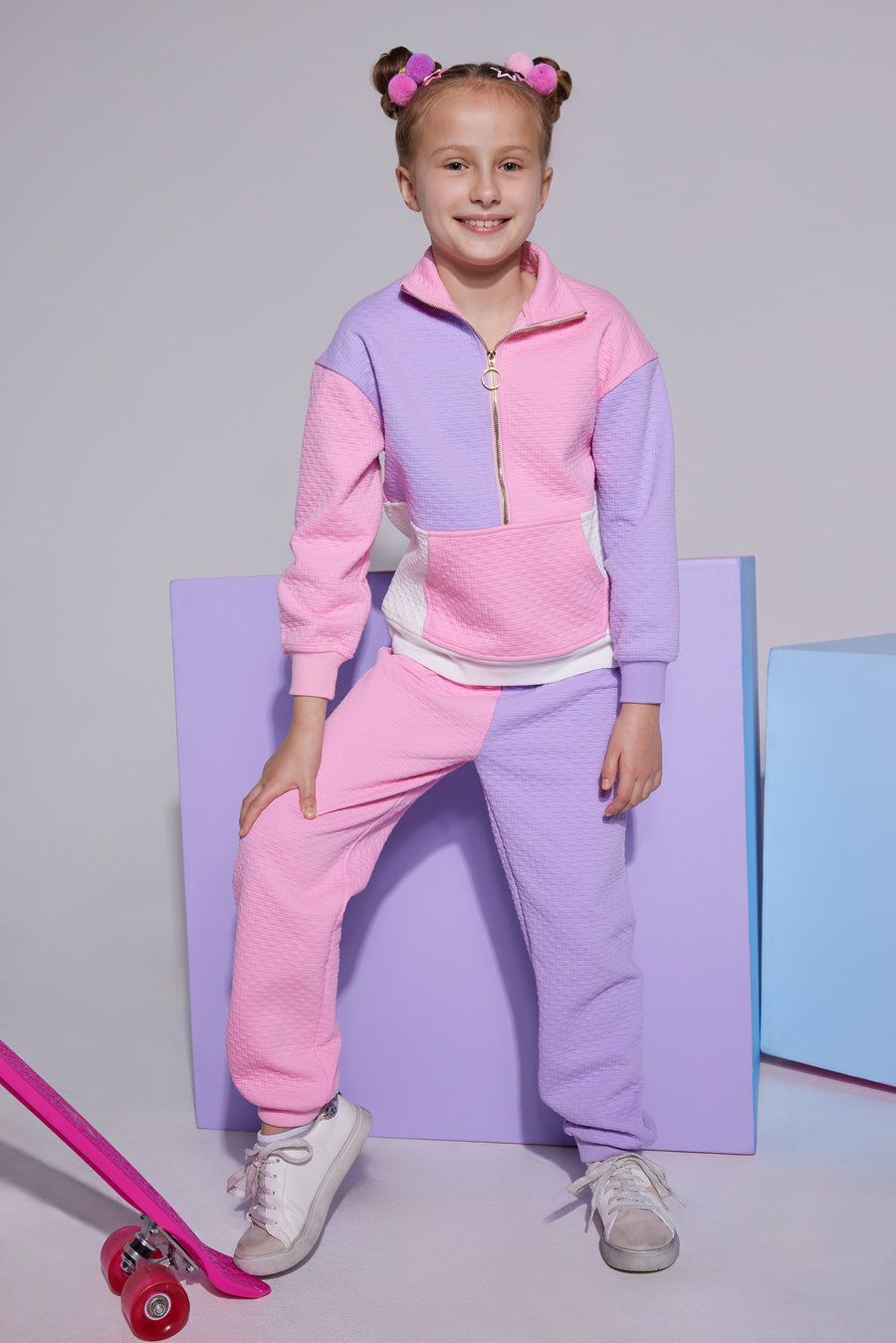 Tween knit jogger pant with elastic waistband that features one pant leg in a light pink and one leg in lilac which pairs back with the matching quarter zip pullover with a gold zipper detail, pocket in the front, and pink/white/purple color block print.