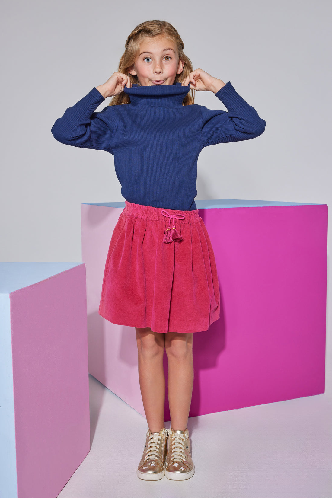 Tween skort in cranberry velvet  which has fixed tie tassels in the front and an elastic waistband seen paired with a navy long sleeve turtleneck.