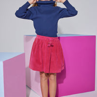 Tween skort in cranberry velvet  which has fixed tie tassels in the front and an elastic waistband seen paired with a navy long sleeve turtleneck.