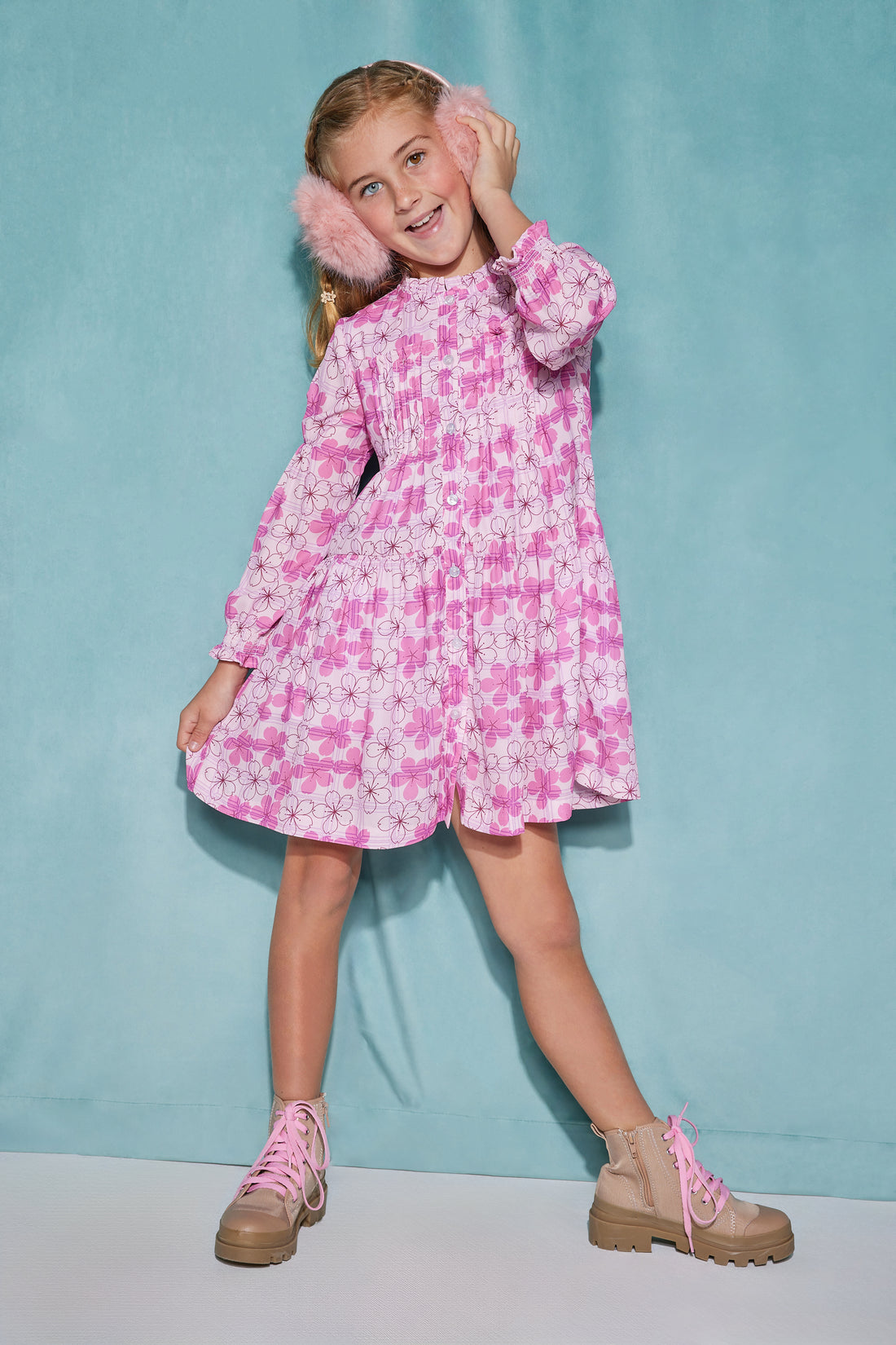 Girl/tween dress made of a lightweight woven fabric that has button closures down the front of the dress and elastic cuffs on the sleeves with a slight ruffle at the neckline. The print features a bright pink Hawaiian floral print