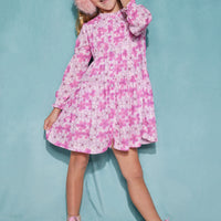 Girl/tween dress made of a lightweight woven fabric that has button closures down the front of the dress and elastic cuffs on the sleeves with a slight ruffle at the neckline. The print features a bright pink Hawaiian floral print