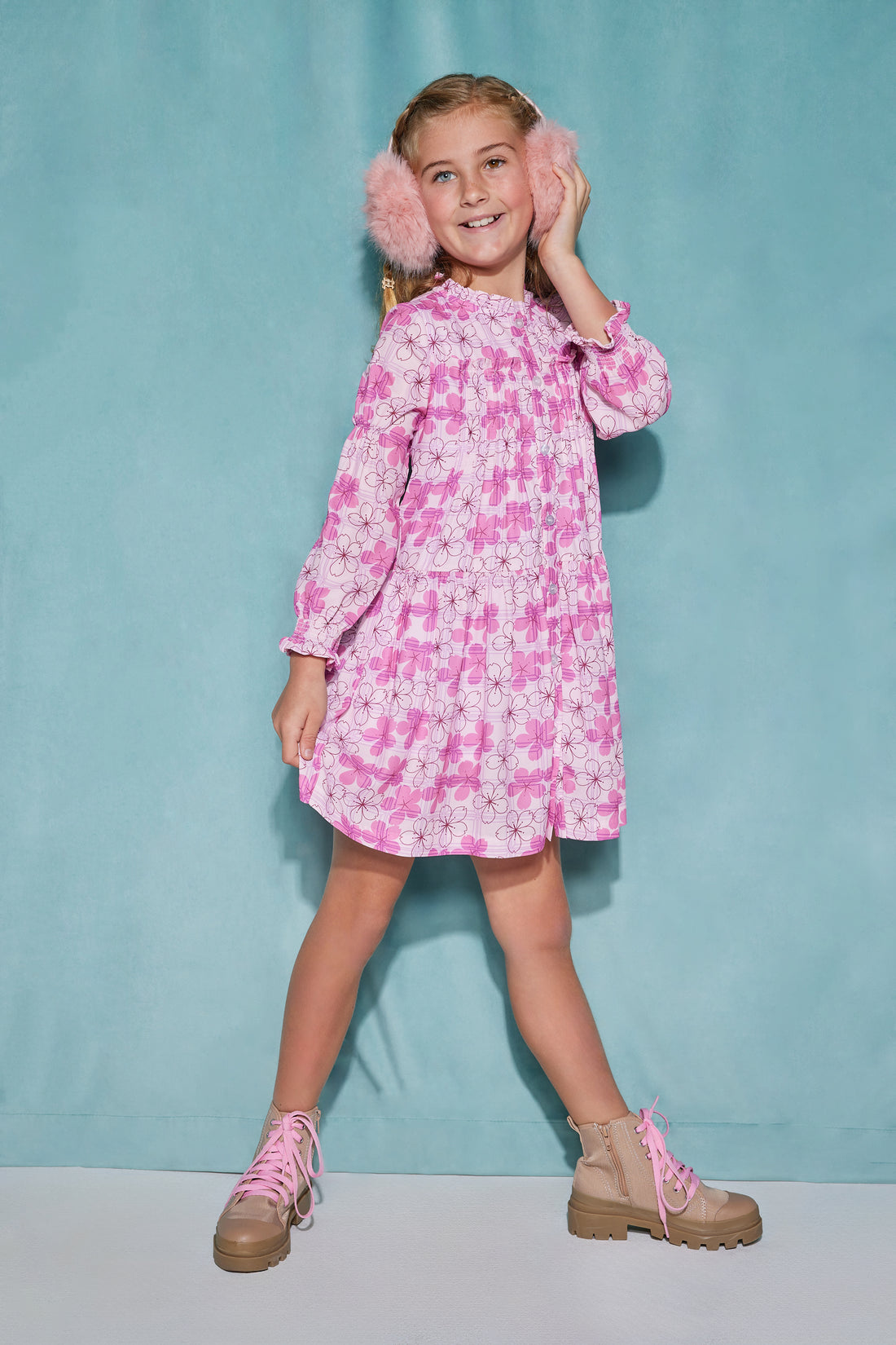 Girl/tween dress made of a lightweight woven fabric that has button closures down the front of the dress and elastic cuffs on the sleeves with a slight ruffle at the neckline. The print features a bright pink Hawaiian floral print