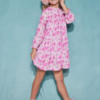 Girl/tween dress made of a lightweight woven fabric that has button closures down the front of the dress and elastic cuffs on the sleeves with a slight ruffle at the neckline. The print features a bright pink Hawaiian floral print