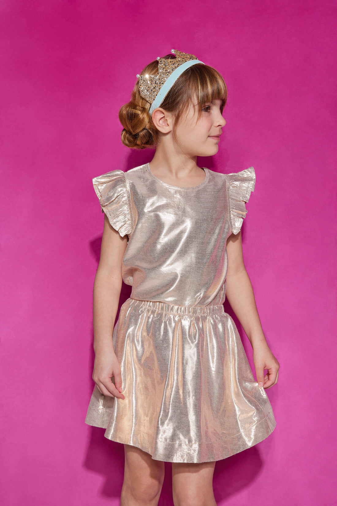 Tween skort with built in shorts and an elastic waistband in a gold metallic color paired back with a gold top featuring a single button closure at back of neck and angel sleeve detail.