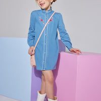 Girls/tween woven faux denim dress that features button closures down the front of dress and a slight ruffle at neckline that also has a red/white/pink embroidery detail at the chest.