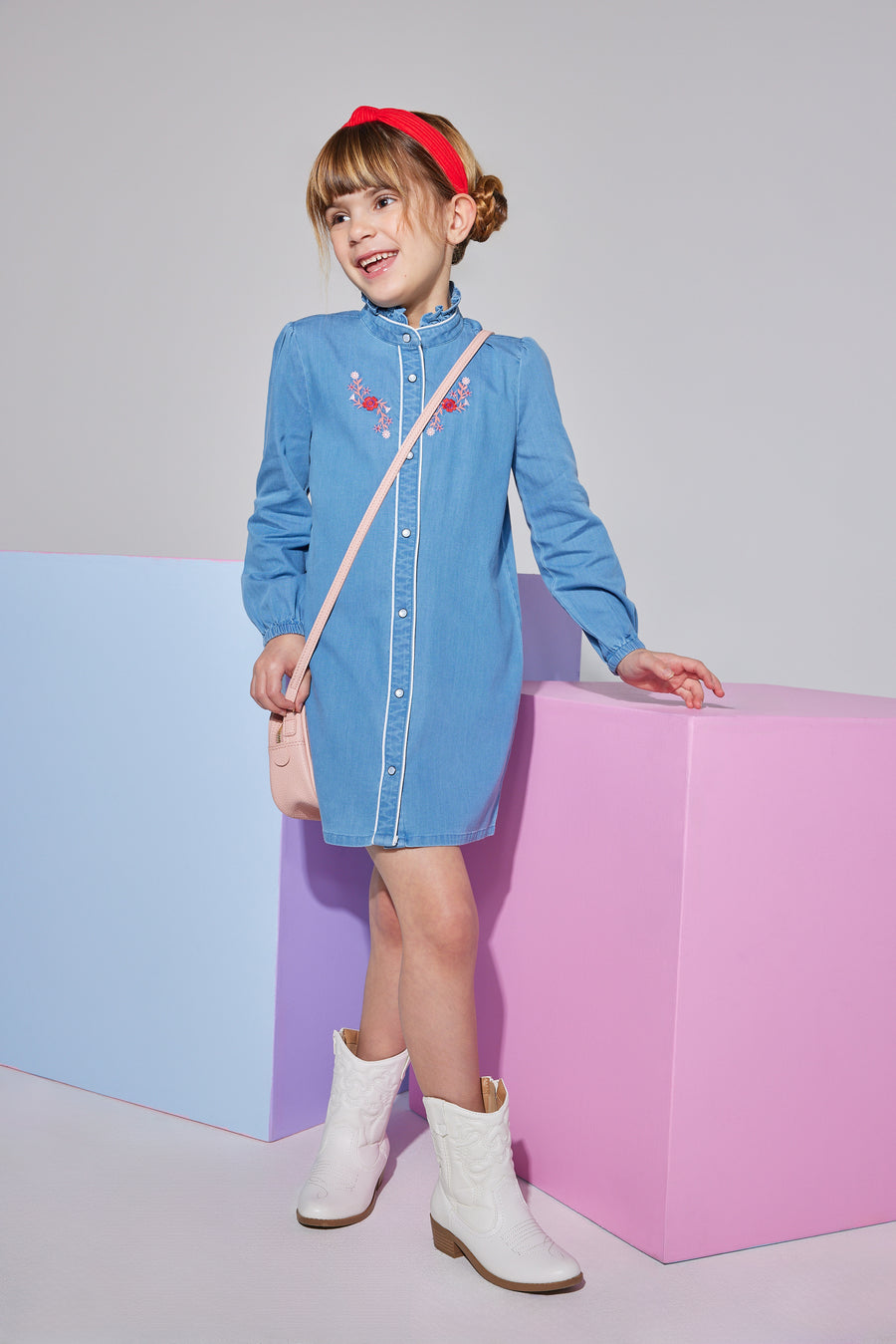 Girls/tween woven faux denim dress that features button closures down the front of dress and a slight ruffle at neckline that also has a red/white/pink embroidery detail at the chest.