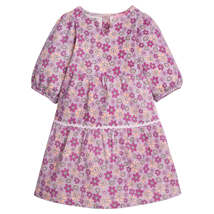 Girls/Tween woven slightly v-neck dress in our Petal floral which features an arrangement of magenta/purple/pink flowers on a light purple background. Dress has a ric rac detail along bottom tier and elastic cuffs on the sleeves. Dress also has button enclosures along the back-BISBY