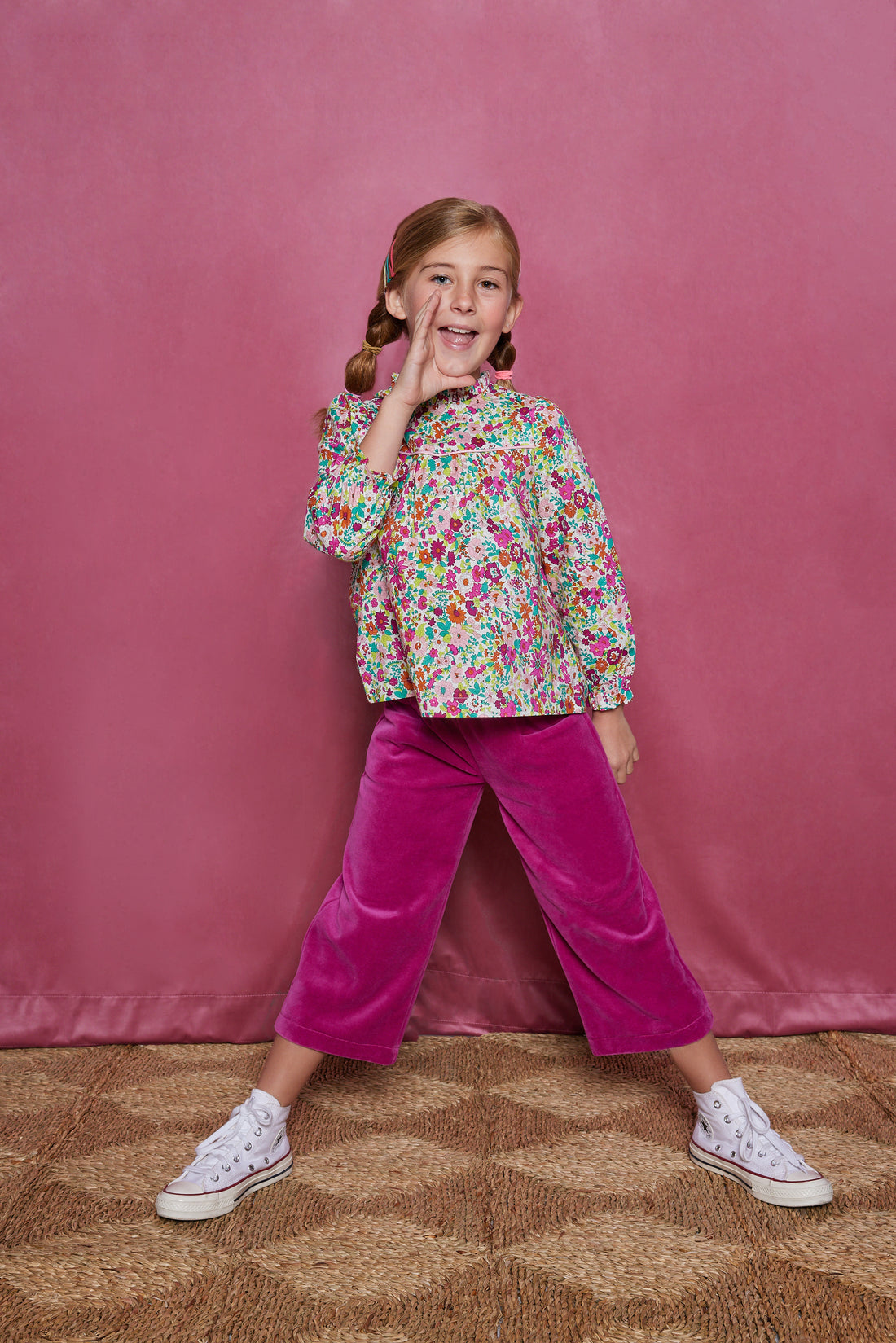 Tween girl cropped magenta velour pants which have pockets in the front and an elastic waistband. Can be seen paired with a long sleeve woven shirt with a ruffle neckline in a magenta/pink/orange/green floral print.