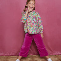 Tween girl cropped magenta velour pants which have pockets in the front and an elastic waistband. Can be seen paired with a long sleeve woven shirt with a ruffle neckline in a magenta/pink/orange/green floral print.