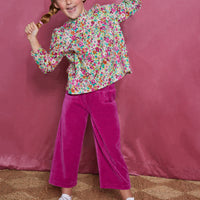 Girls/tween woven long sleeve top  in a magenta/pink/orange/green floral pattern which features a ruffle neckline, elastic cuffs at end of sleeves, and slight gathering across bust for a relaxed comfy fit. These tops pair back greatly with our velour pants in the magenta color to complete the look.