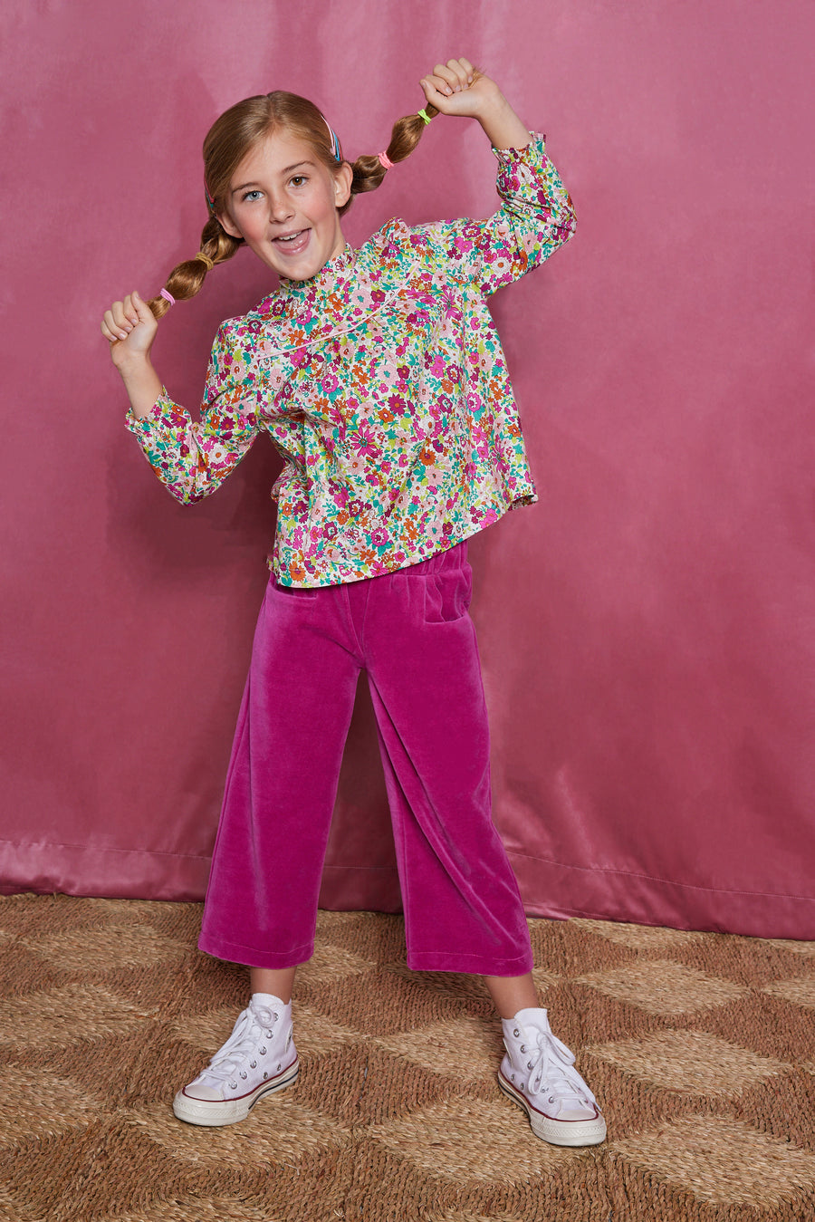 Girls/tween woven long sleeve top  in a magenta/pink/orange/green floral pattern which features a ruffle neckline, elastic cuffs at end of sleeves, and slight gathering across bust for a relaxed comfy fit. These tops pair back greatly with our velour pants in the magenta color to complete the look.