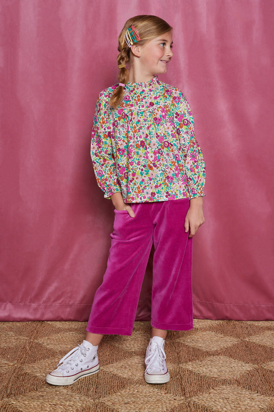 Tween girl cropped magenta velour pants which have pockets in the front and an elastic waistband. Can be seen paired with a long sleeve woven shirt with a ruffle neckline in a magenta/pink/orange/green floral print.