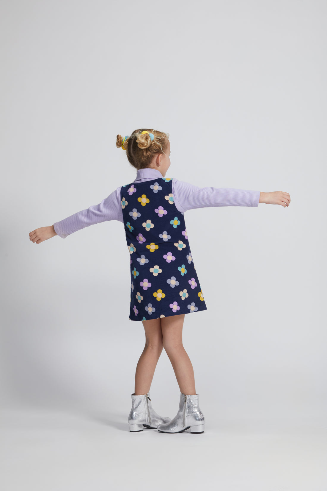 Girls/Tween jumper in a lightweight corduroy material. Jumper has a zipper down the front, pockets, and can be seen in a purple/blue/yellow floral arrangement on a navy background. Perfect as a layering piece, as seen model is wearing a ribbed turtleneck in lilac which pulls back in nicely with the jumper.