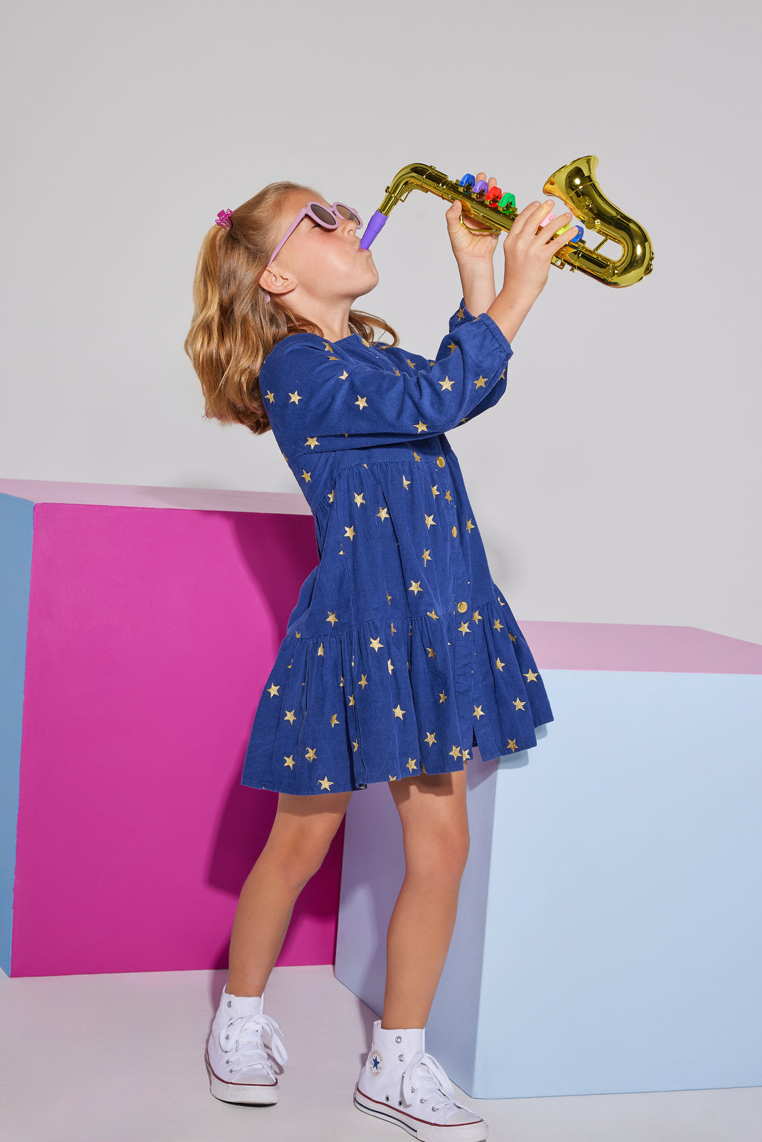 Girls/Tween corduroy dress in a navy color with gold stars printed on it. Dress features gold button closures down the front of dress, elastic cuffs at sleeves, and a slight ruffle detail at bust