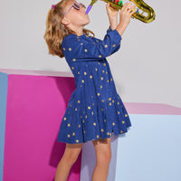 Girls/Tween corduroy dress in a navy color with gold stars printed on it. Dress features gold button closures down the front of dress, elastic cuffs at sleeves, and a slight ruffle detail at bust