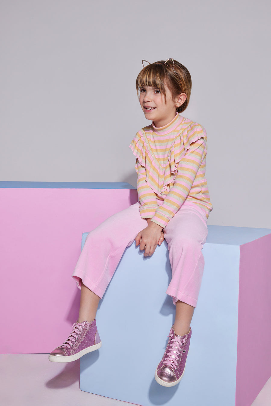 Girl/Tween cropped velour pants in the light pink velour shade. Pants feature a soft velour material, with pockets in the front, and an elastic waistband for a comfy fit. Model can be seen wearing a knit top with angel sleeves in a pastel stripe pattern to complete the look. 